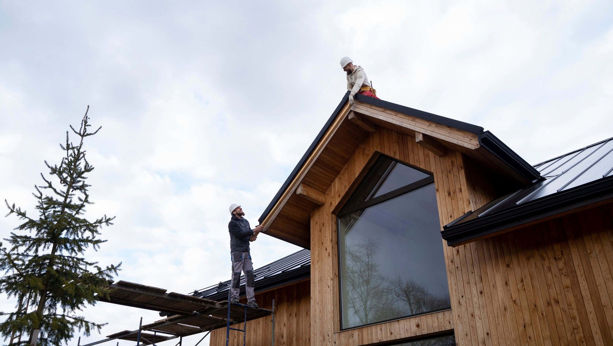 Håndverkere arbeider på tak med stillas og sikkerhetsutstyr under byggeprosess.